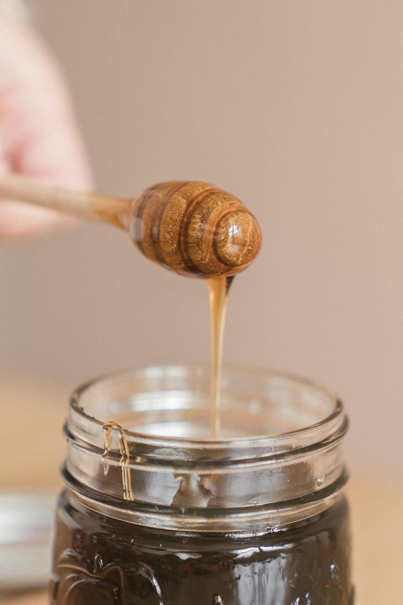 About 3 A close-up of honey dripping from a wooden dipper into a glass jar, showcasing its rich texture.