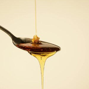 Close-up of golden honey flowing from a spoon against a soft yellow backdrop, capturing its sweet allure.