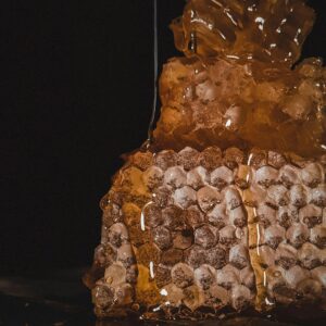 Close-up of natural honeycomb with golden honey dripping on a dark background.