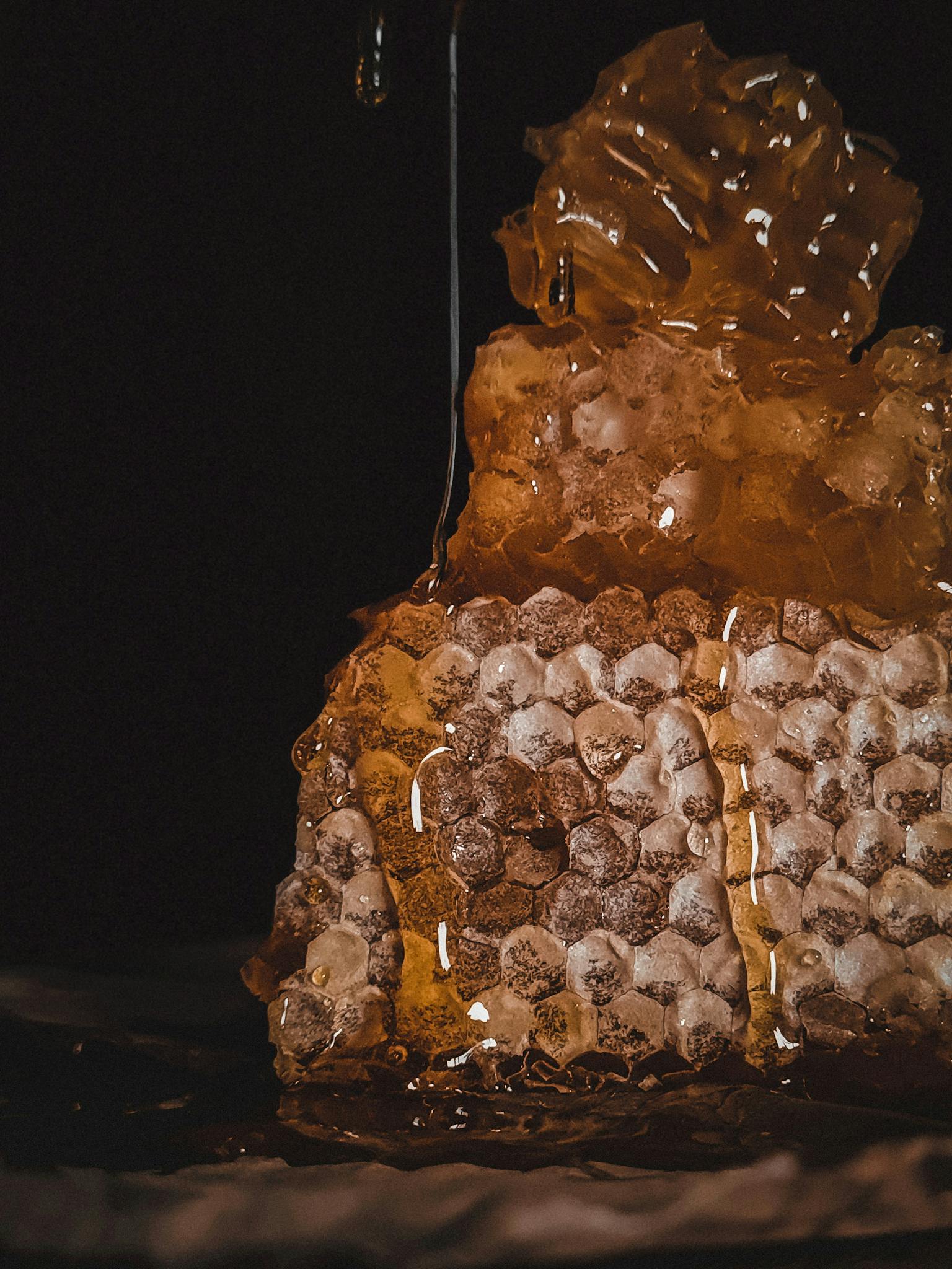 Close-up of natural honeycomb with golden honey dripping on a dark background.