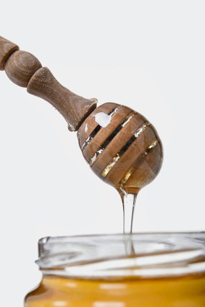 Sweet golden honey flowing from a wooden dipper, highlighting its thick, sticky texture.