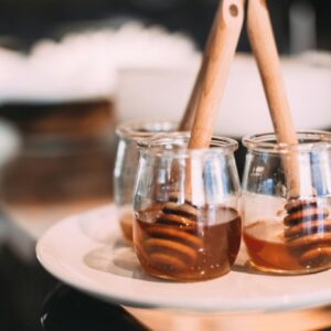Three glass jars filled with honey and wooden dippers, elegantly displayed on a white plate.