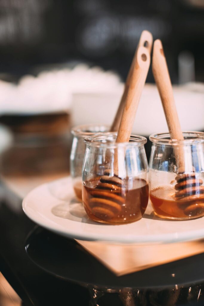 Three glass jars filled with honey and wooden dippers, elegantly displayed on a white plate.