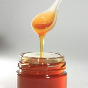 Vibrant close-up of golden honey drizzling from spoon into jar, showcasing its sticky texture.