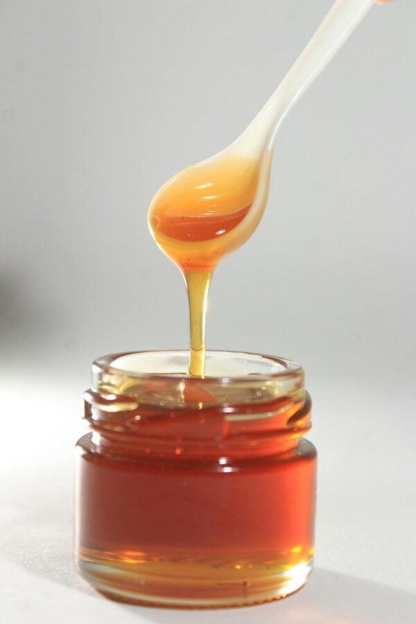 Vibrant close-up of golden honey drizzling from spoon into jar, showcasing its sticky texture.