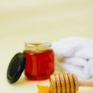 Warm-toned still life featuring golden honey in a jar with a wooden dipper on a soft background.